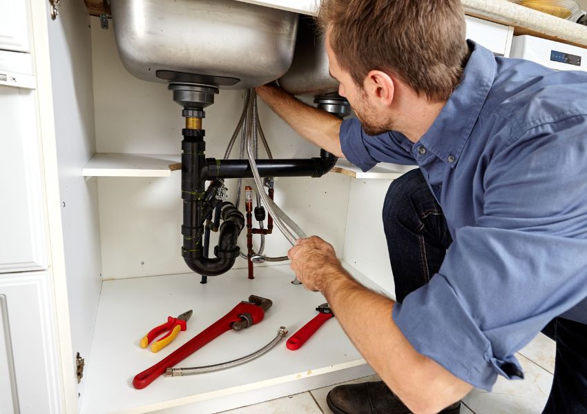 plumber using a wrench to fix a leaking backroom sink